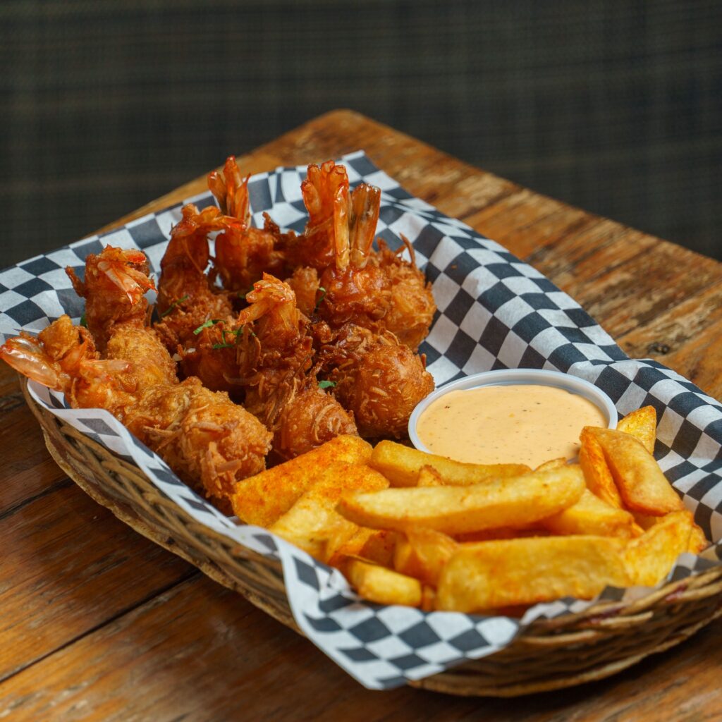 Golden fried shrimp and fries served in a basket with dipping sauce on a rustic wooden table.
